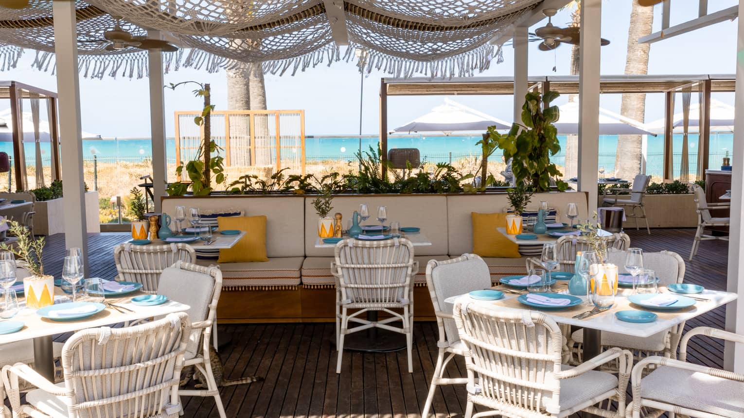 Restaurant terrace with white dining seating and banquettes with sea view in backdrop