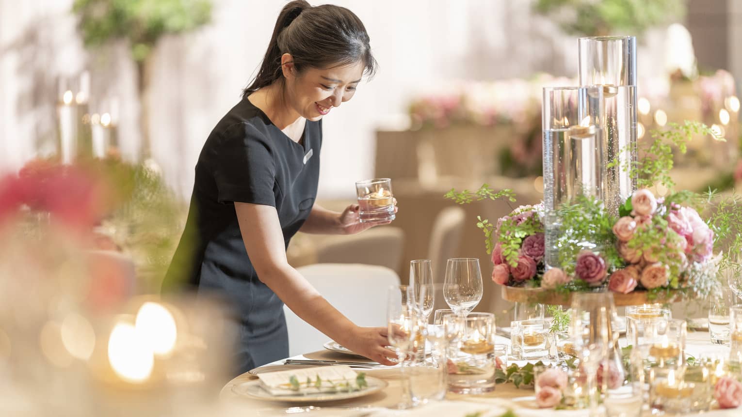 Smiling FS staff member sets table in ballroom with pink flower centrepiece