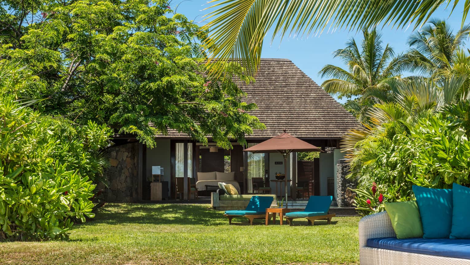Beach Pool Villa behind green lawn with blue patio chairs, tropical plants