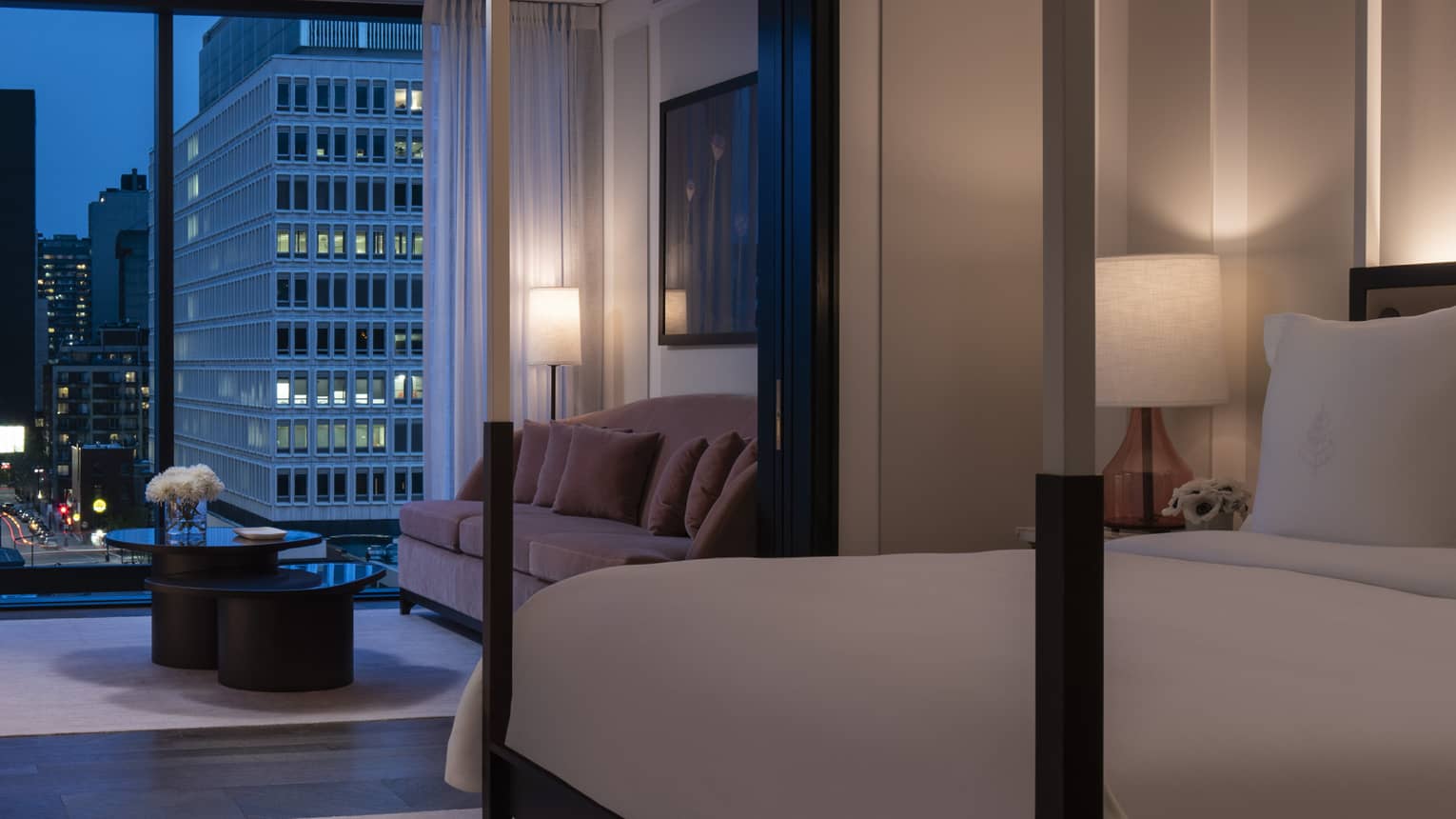 Presidential Suite dimly lit and with all-white modern four-poster bed and evening balcony view