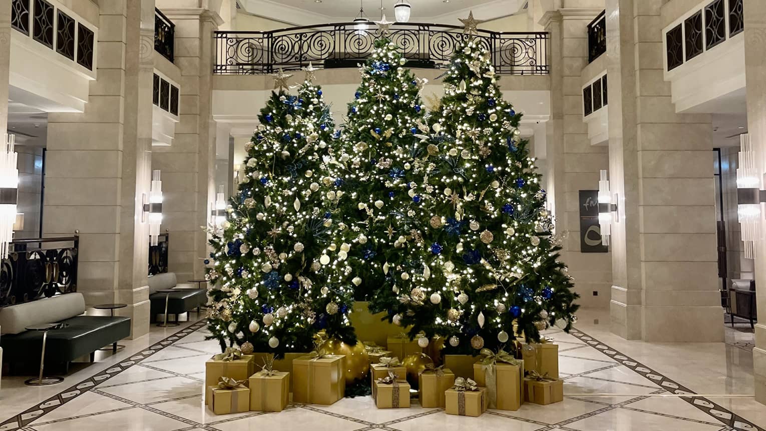 Three Christmas trees decorated in gold sit in the center of the Hotel lobby, with gold-wrapped boxes of presents beneath each one