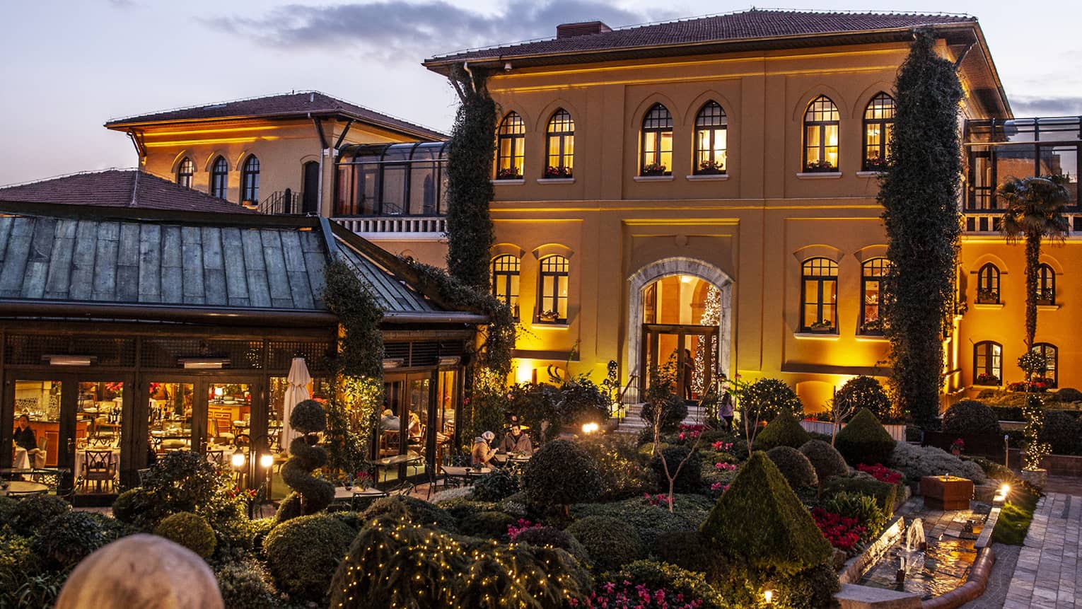 A courtyard at dusk, with the warm glow of the lights on in Hotel in the background