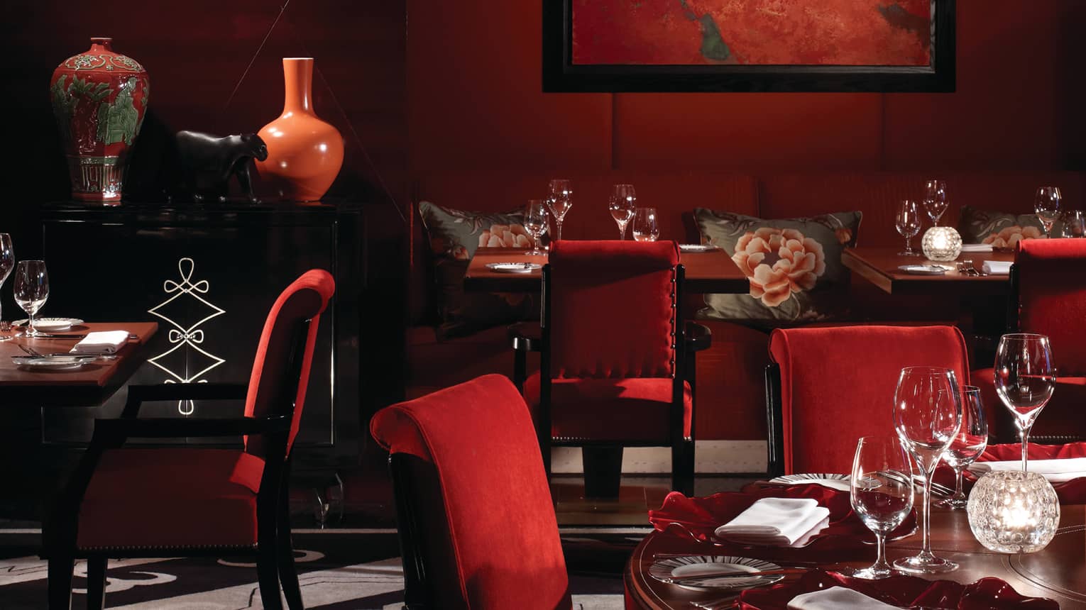 Amaranto restaurant red velvet chairs, tables, floral vases and pillows on banquettes