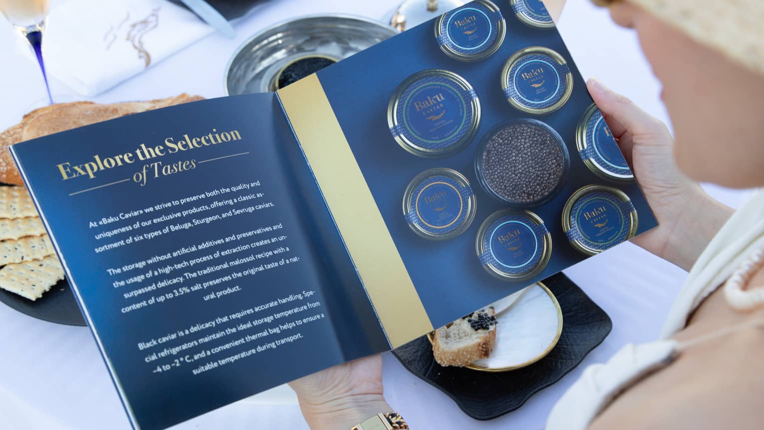 A guest in a straw hat peruses a caviar menu at a patio table arrayed with full bowls, plates and glasses of sparkling wine.