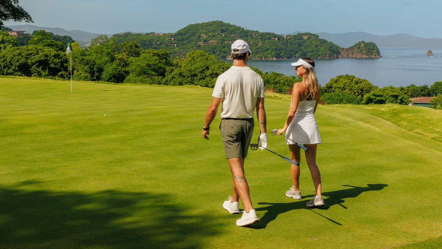 Two golfers walk side by side along a greenway with the ocean in the background