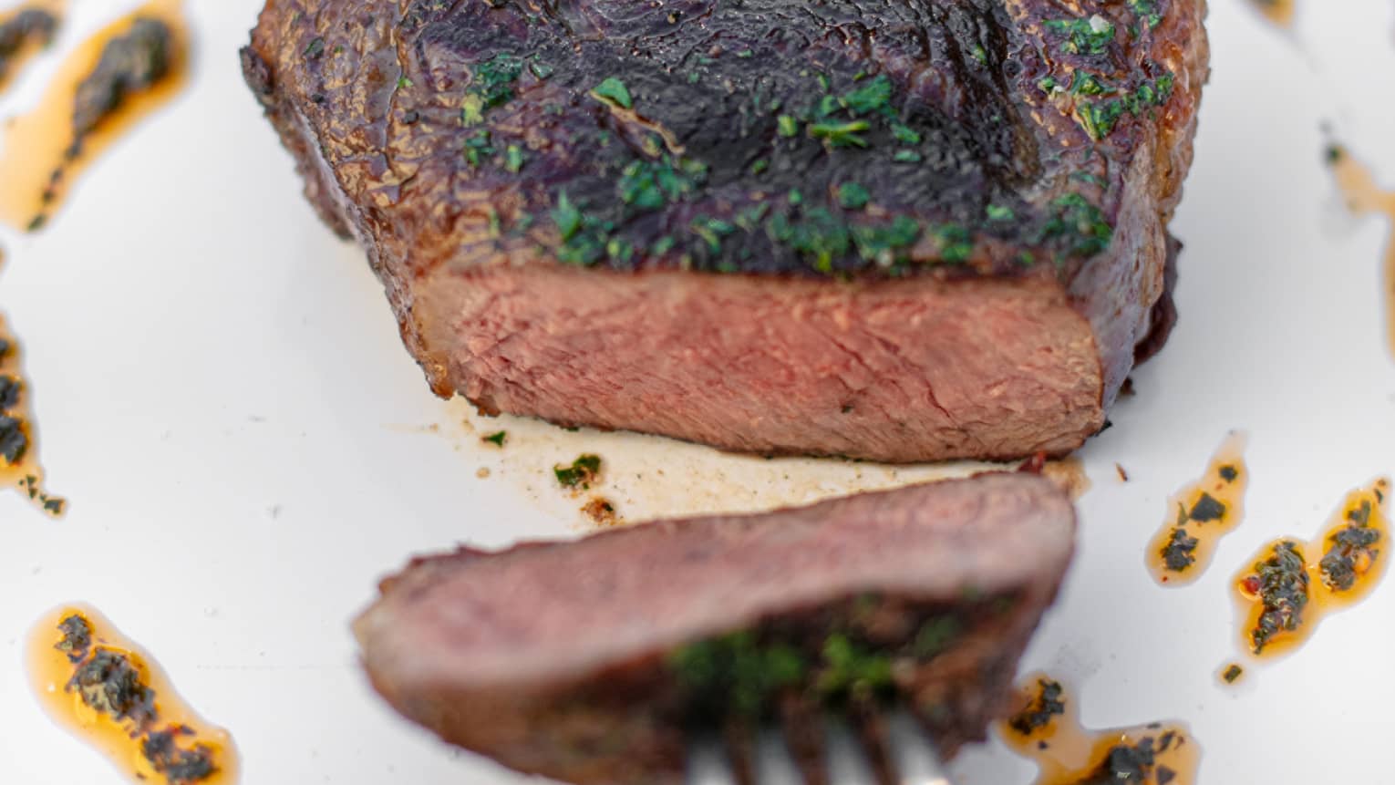 A fork pulling a piece of sirloin across a plate.