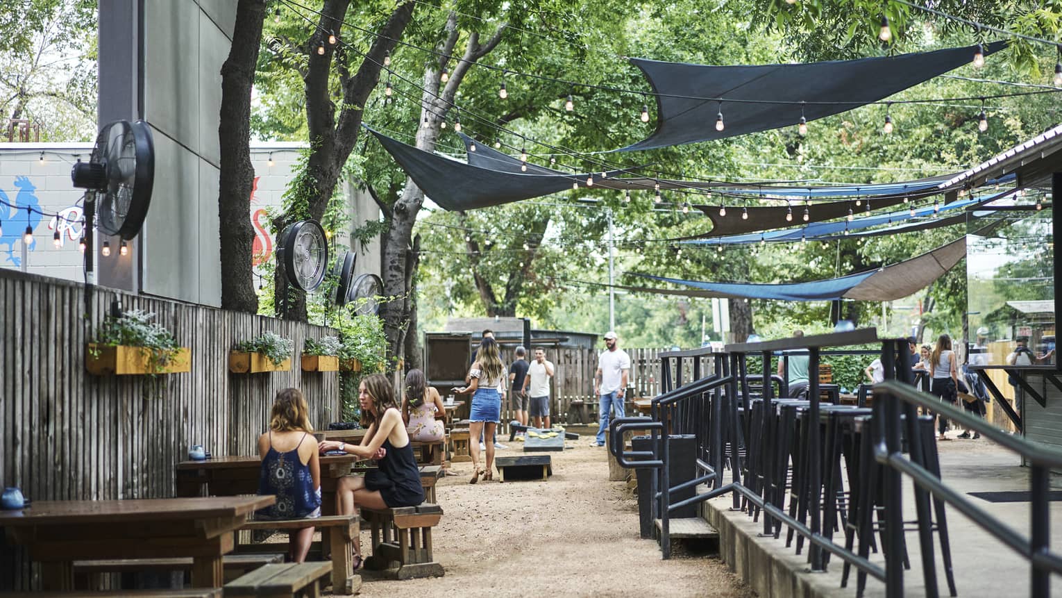 Groups of friends socialize in large outdoor Rainey Street bar under fabric overhangs, lights during day