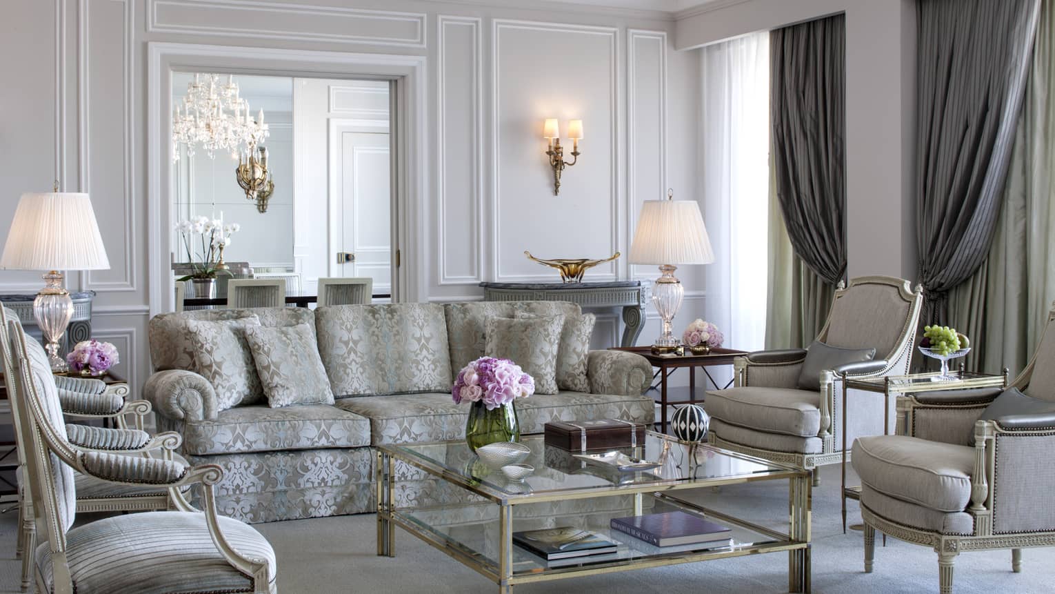 Royal Suite bright, elegant living room with blue-and-grey satin sofa, armchairs, glass coffee table with gold trim, white walls