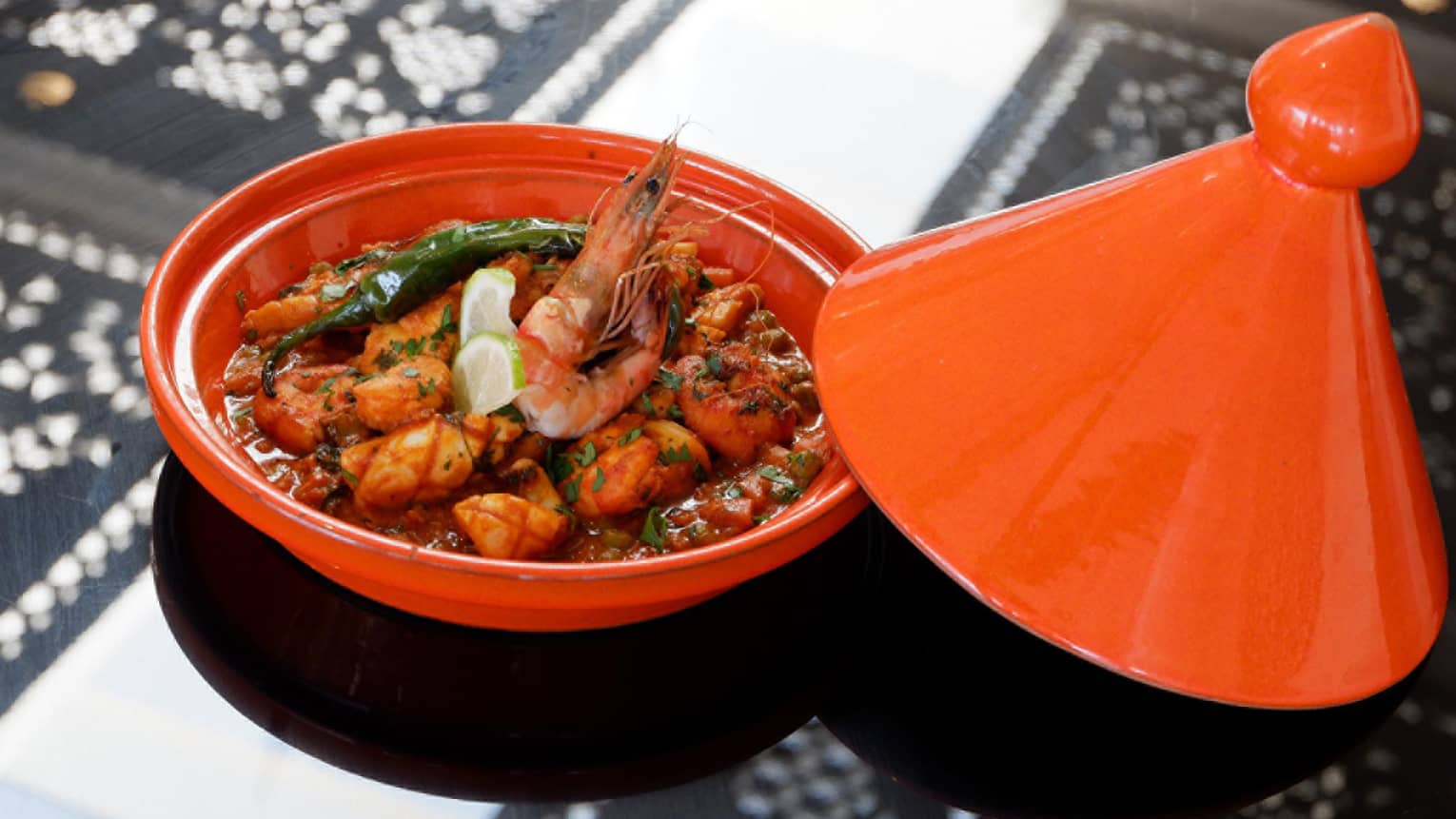 Seafood Tagine fresh fish, prawns in red sauce with lime wedge garnish in red tagine 