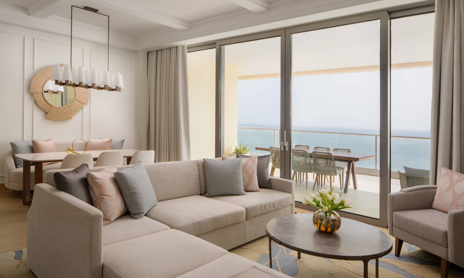 Contemporary living and dining area with neutral tones, a sectional sofa and large glass doors opening to a balcony with ocean views.,Contemporary living and dining area with neutral tones, a sectional sofa, and large glass doors opening to a balcony with ocean views.