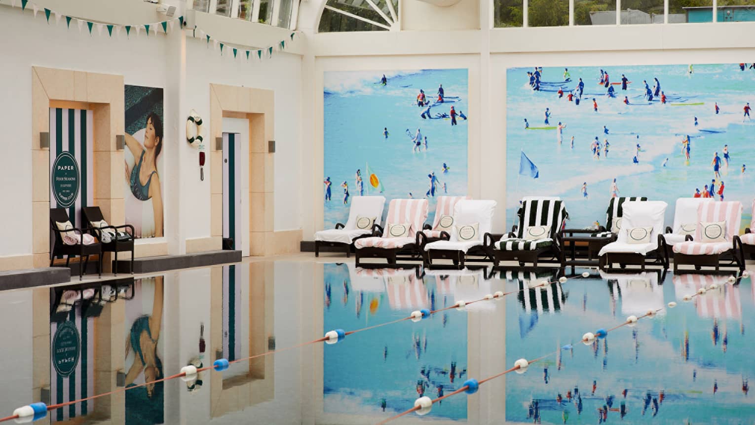 Indoor spa pool with striped lounge chairs along wall with lively blue wallpaper