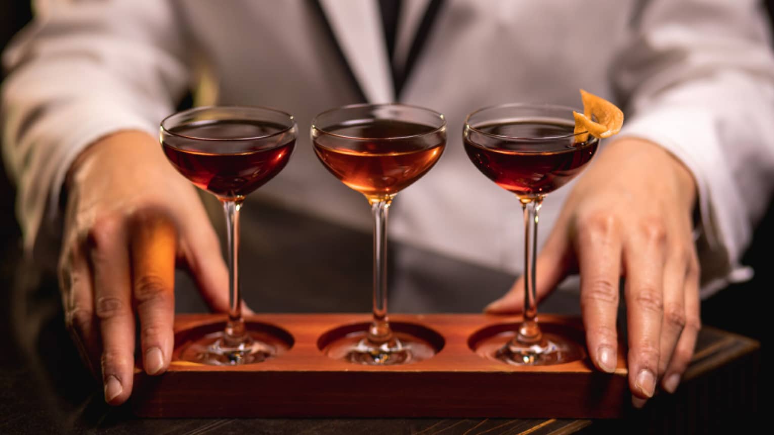 A bartender displays three cocktails in glasses
