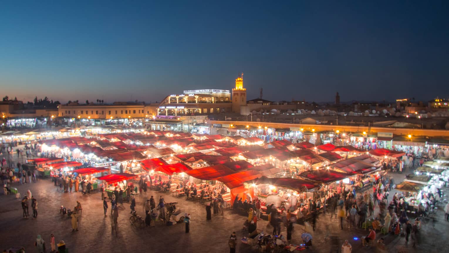 Looking down at outdoor night market, people gathered around tents, stalls, lights
