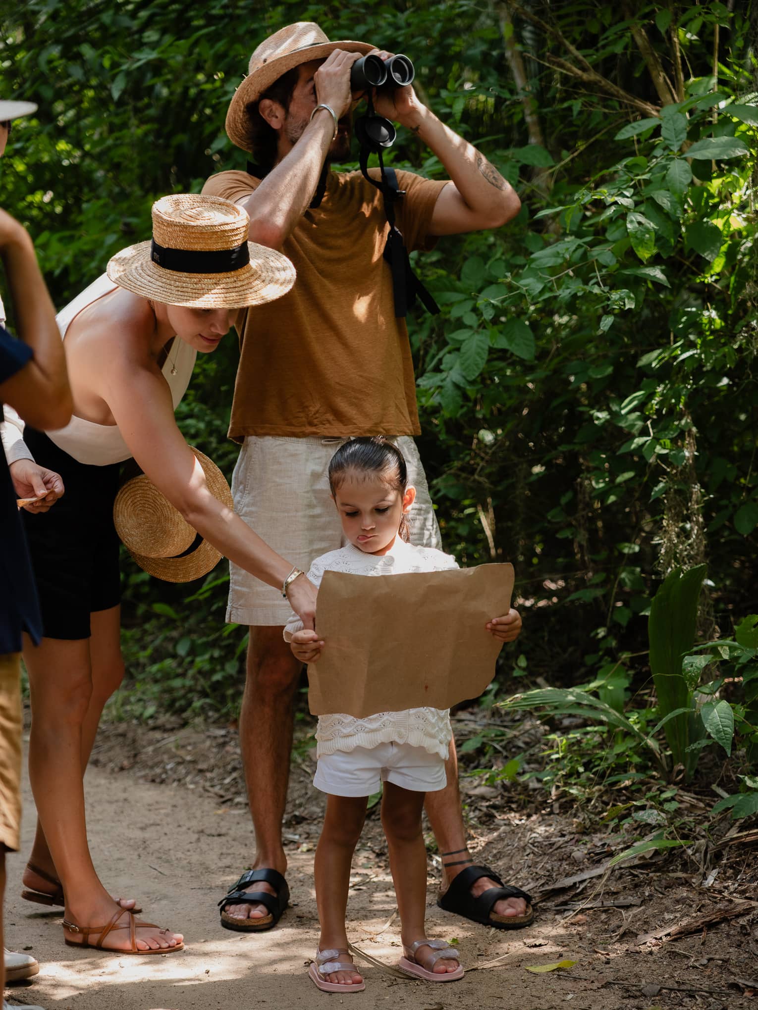 A group of people on a jungle trail. Two are consulting a map, and one is looking through binoculars.