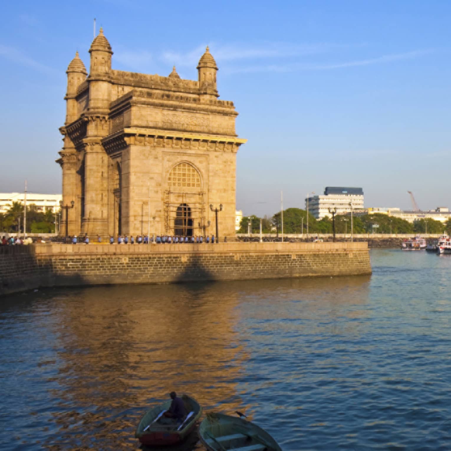 Harbourside view of an imposing towered stone structure, scattered rowboats in the foreground, larger moored ships beyond.