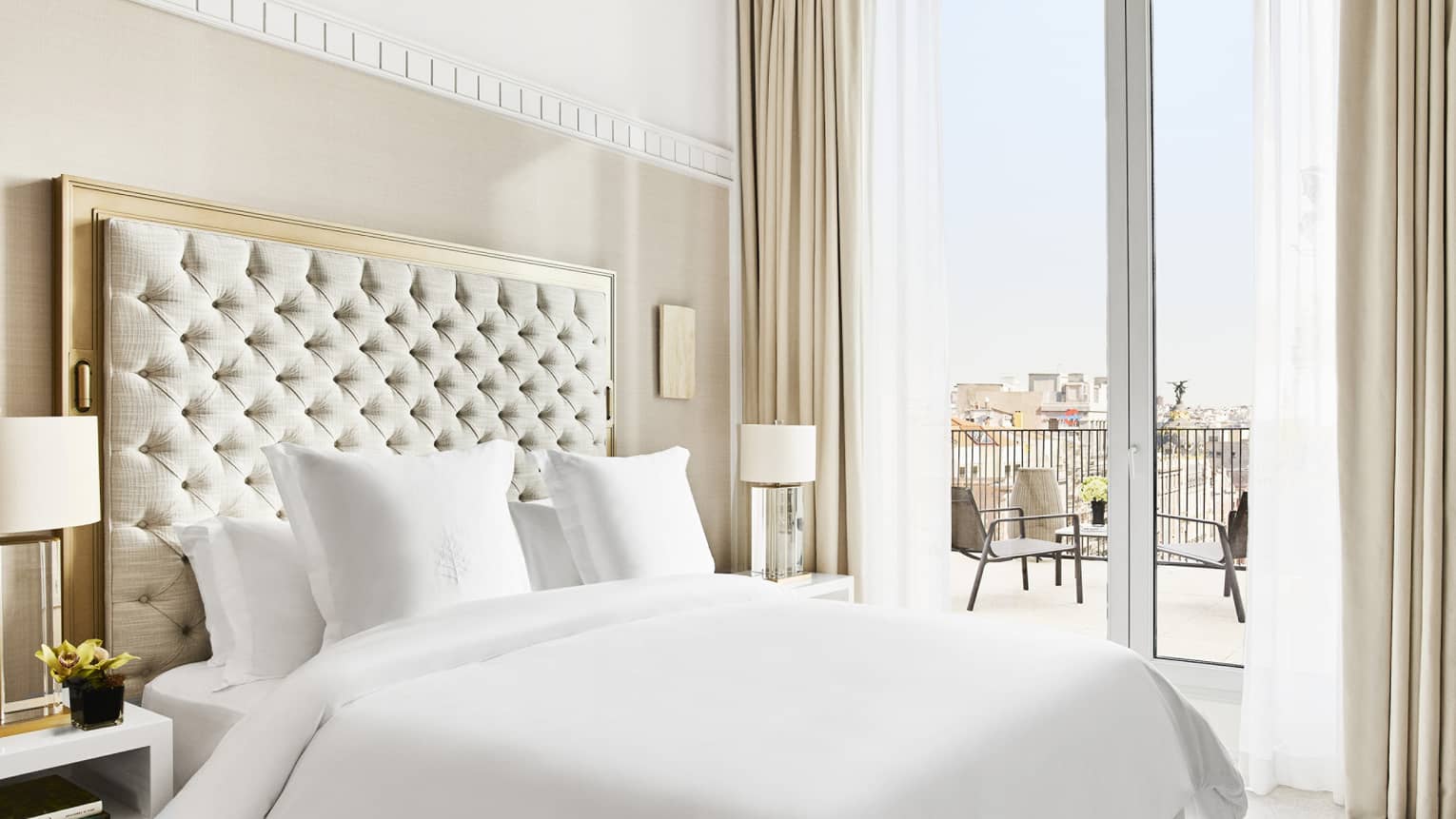 Luxury hotel suite bedroom with a king bed, tufted headboard, bedside lamps and access to a private terrace with city views