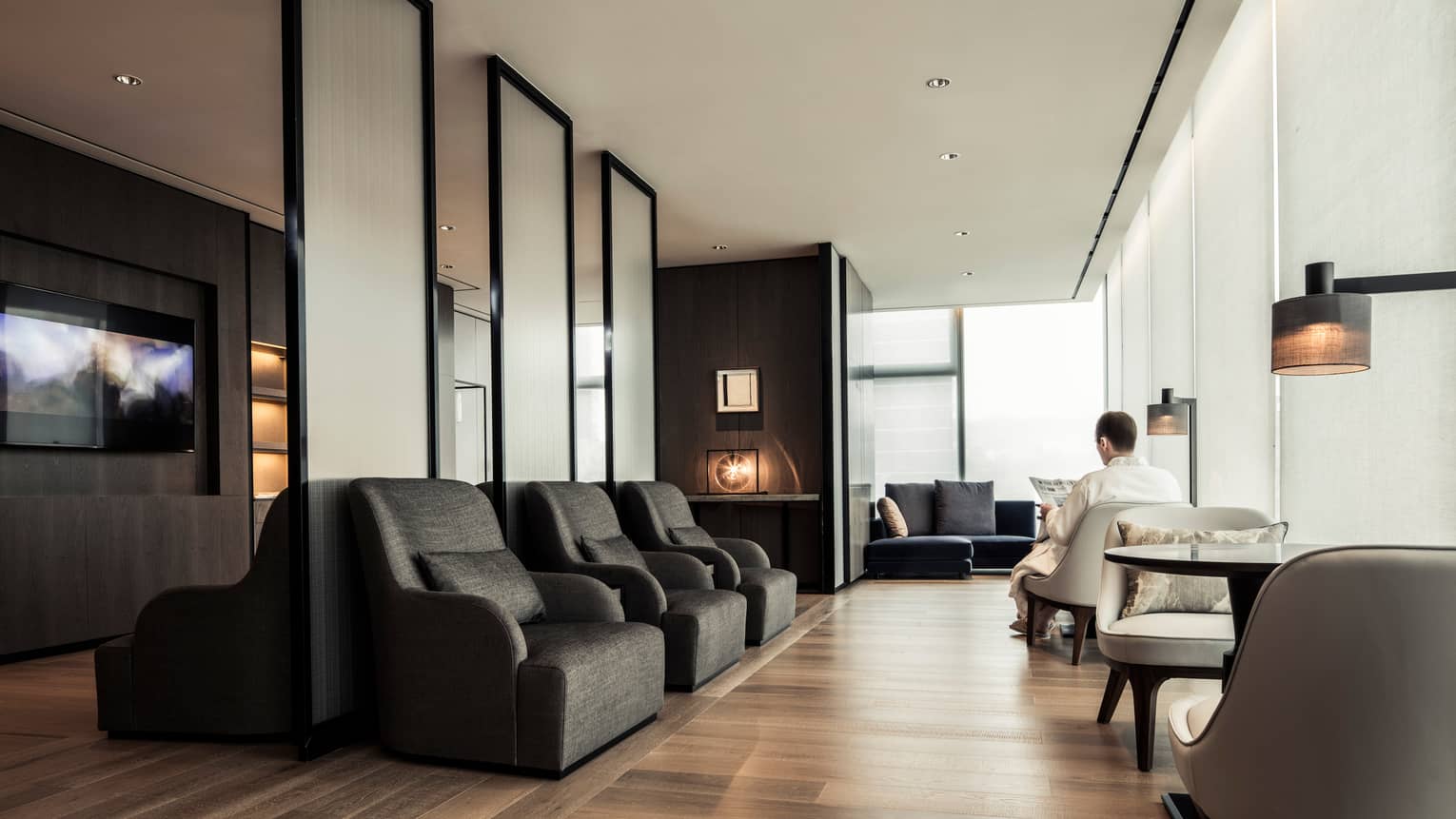 Man wearing white bathrobe reads newspaper among armchairs, tables in sunny Relaxation Room