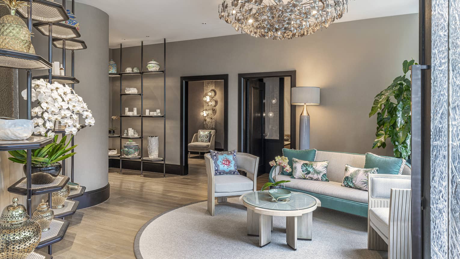 Spa lobby with cream and teal sofa, armchair, glass-top coffee table, floor-to-ceiling shelves with spa products, intimate lighting