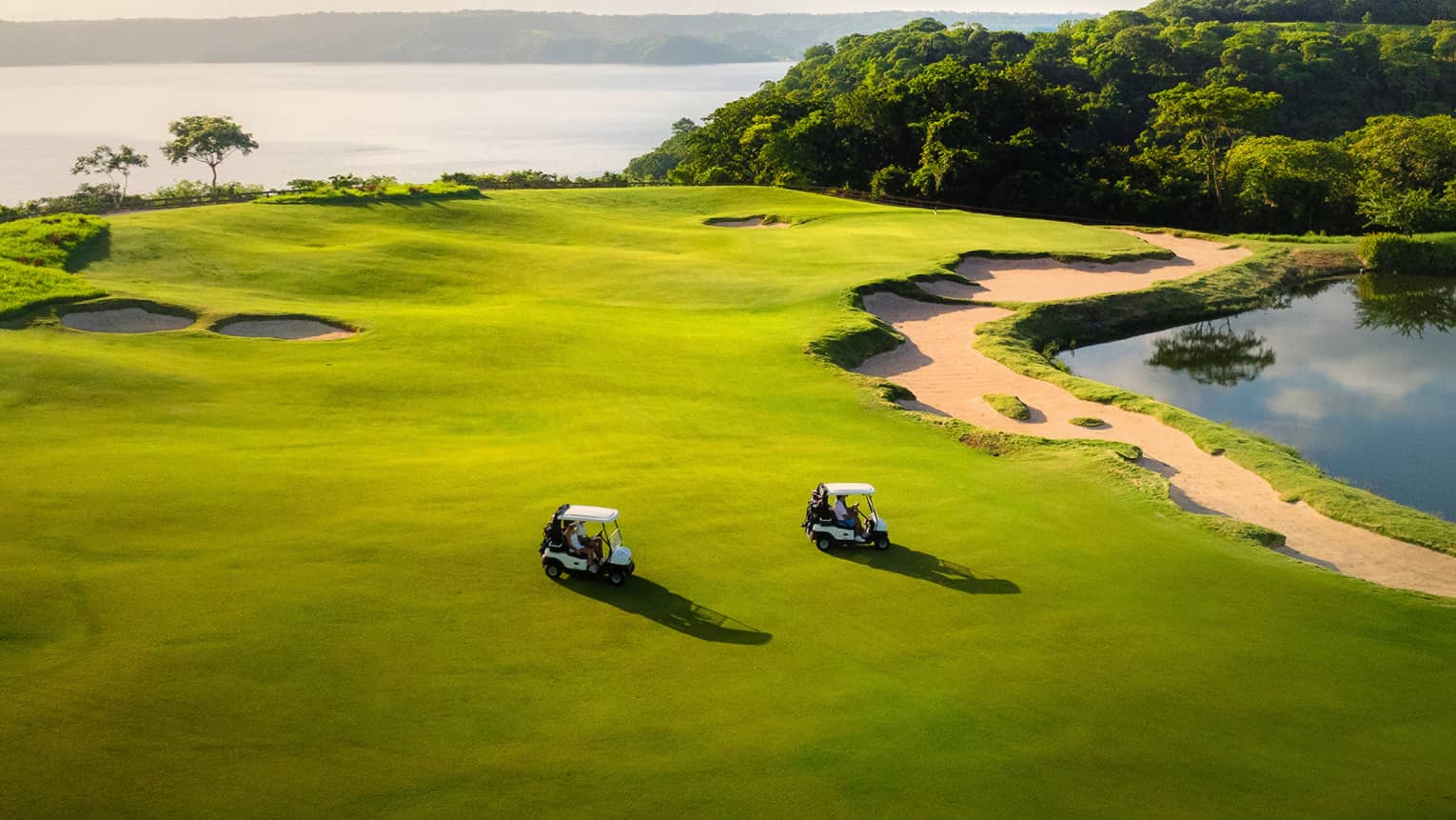 Two golf carts ride along a green with the ocean in the background