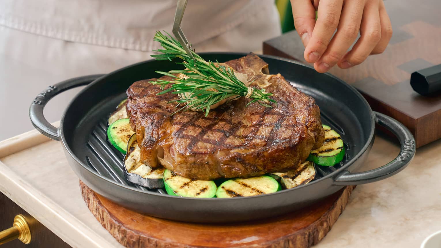 Chef places sprig of rosemary onto grilled piece of beef with kitchen tweezers