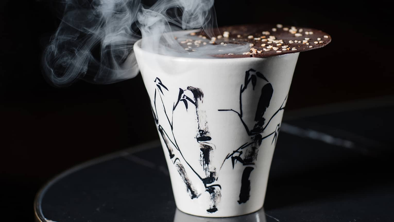 Black-and-white fluted ceramic cup topped with thin chocolate cookie and emitting smoke