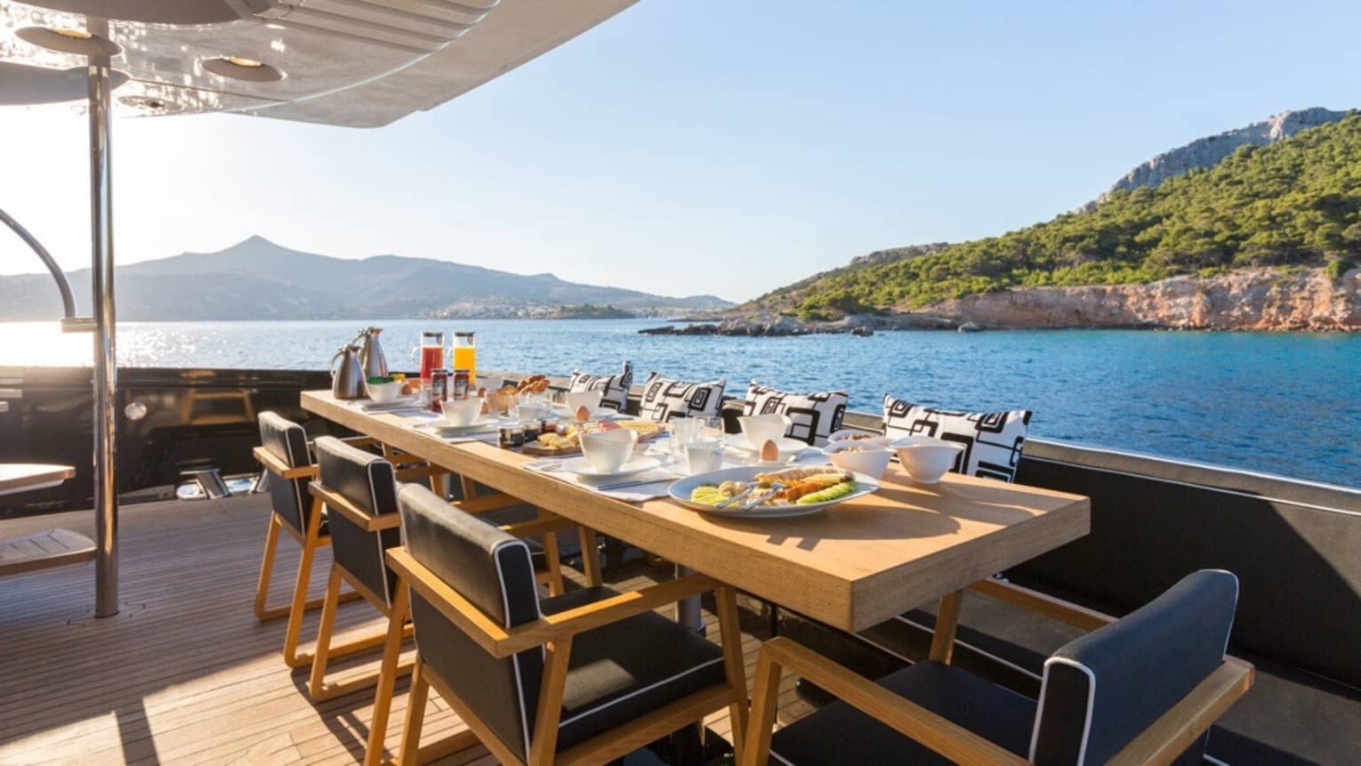 Dining setup on yacht deck overlooking blue water and lush landscape