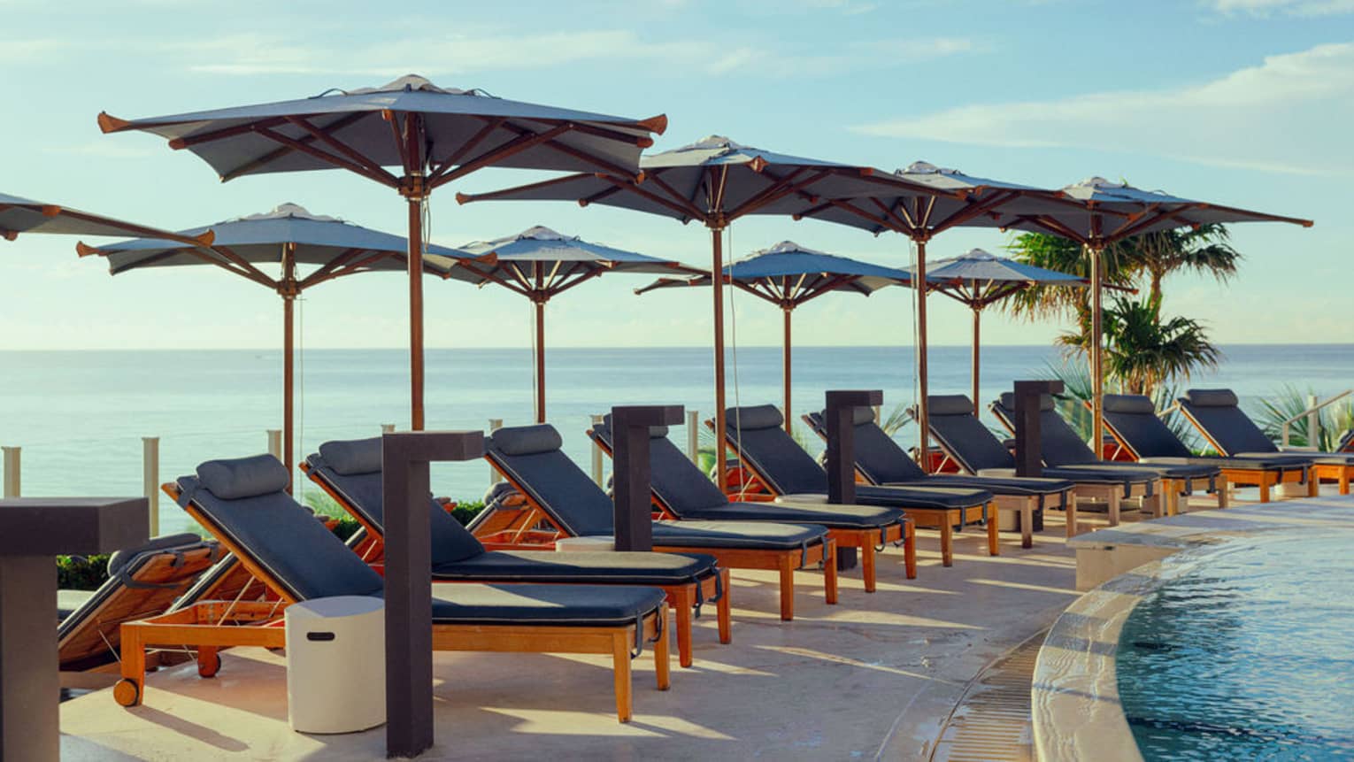 Rows of lounge chairs and umbrellas near a pool with the ocean in the background