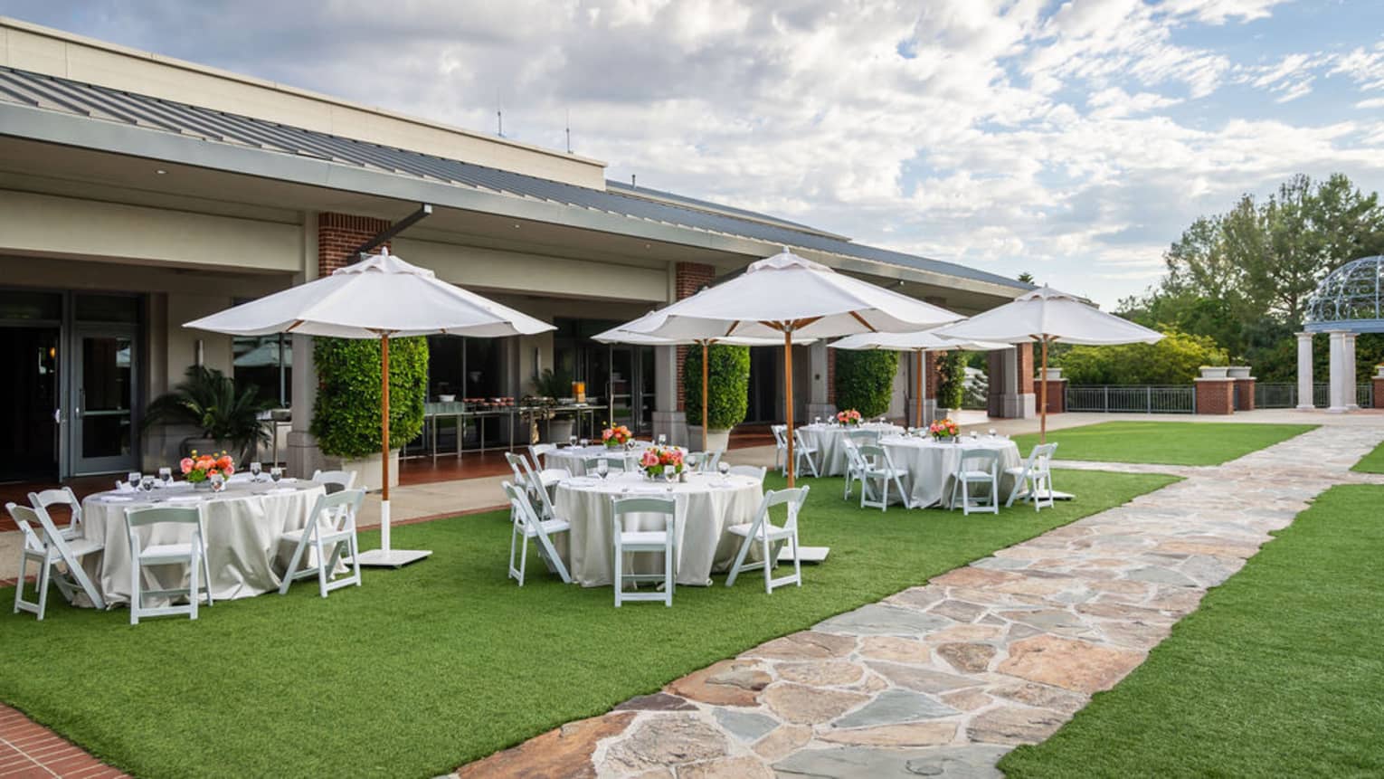 Outdoor lawn set with white umbrellas and round tables covered in white linens