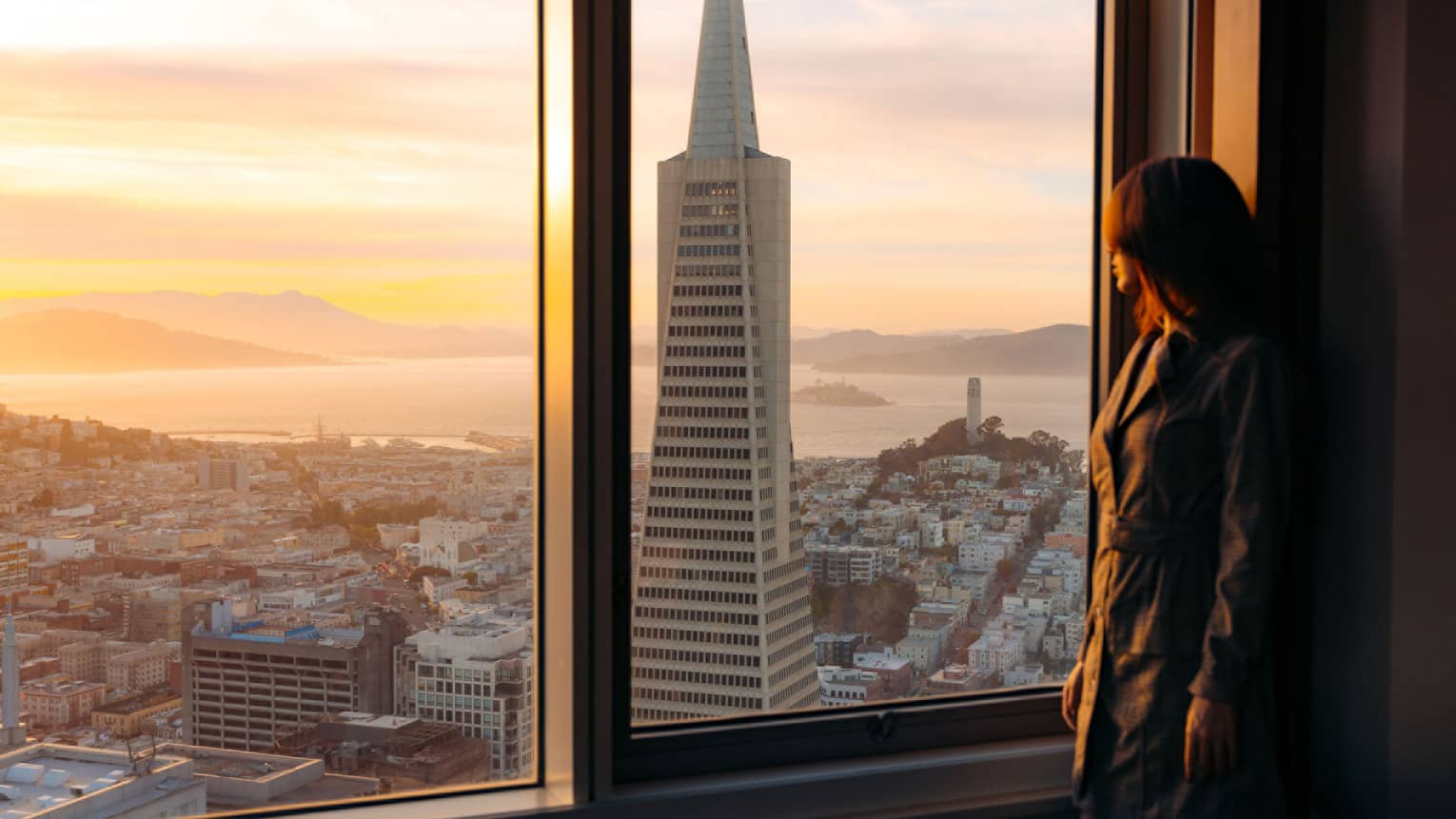 Woman gazes out hotel window to San Francisco cityscape