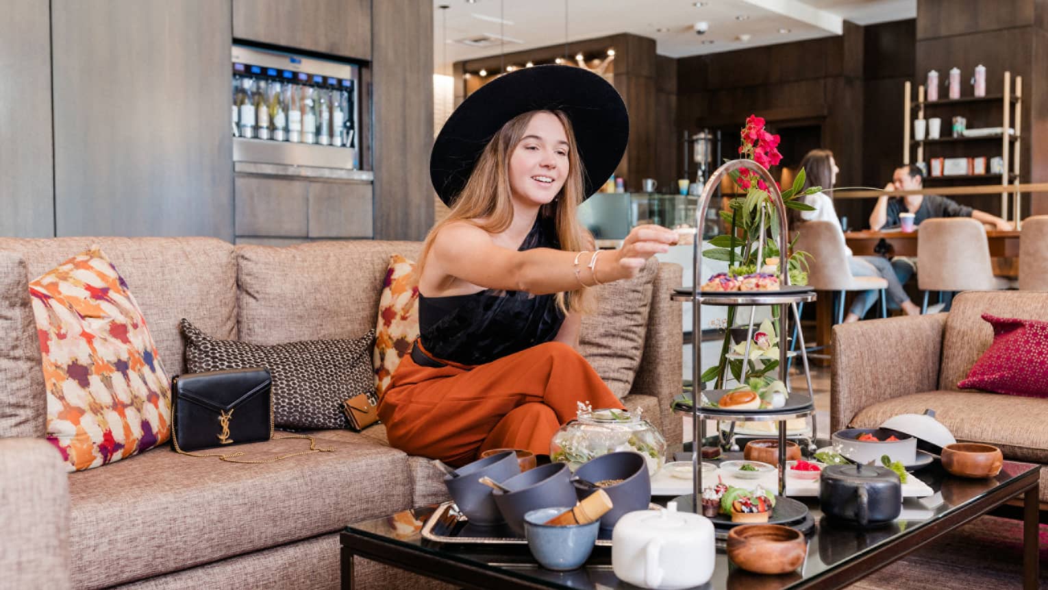 A woman in a large black hat enjoying an afternoon tea.