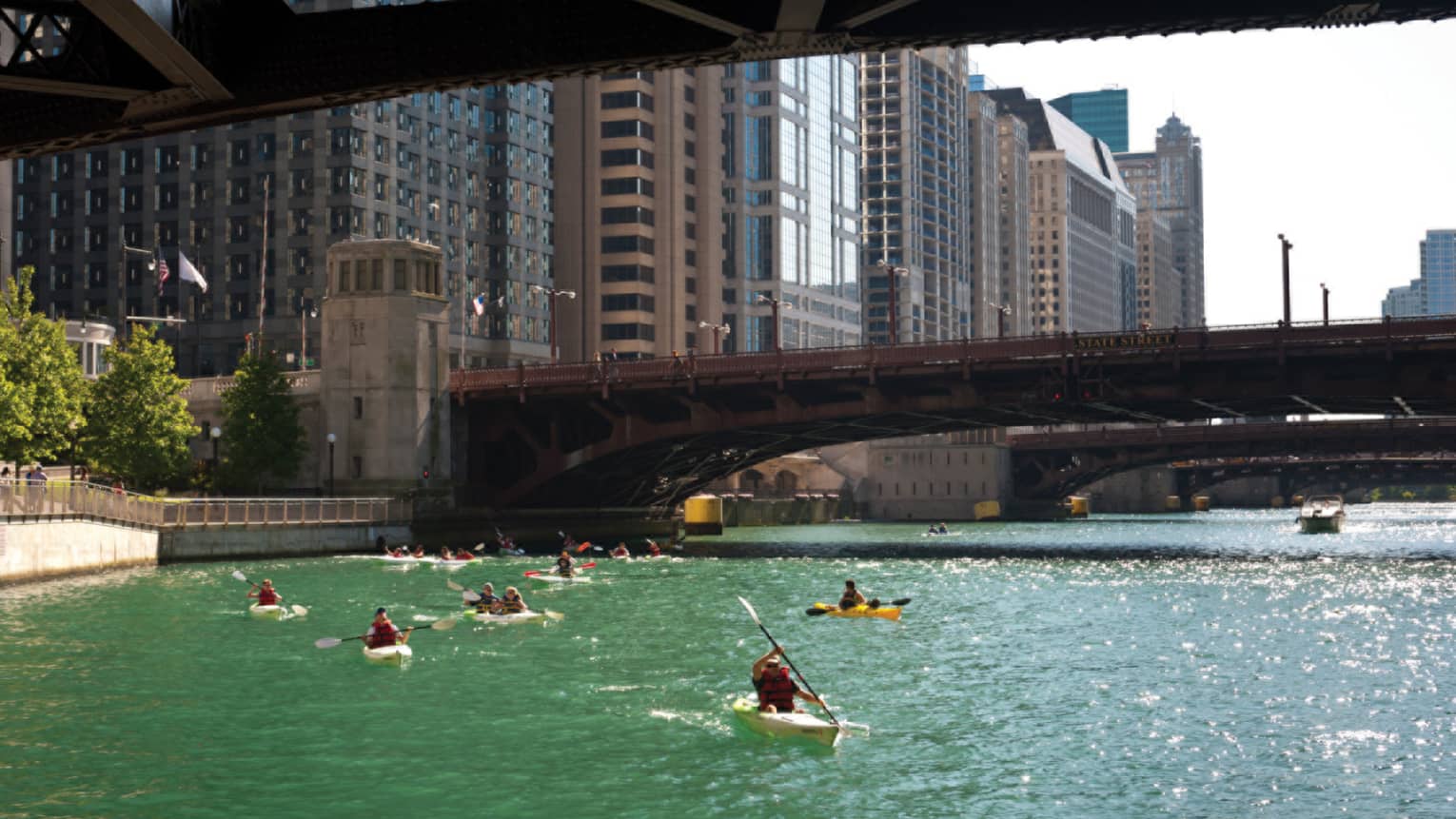 People kayaking on a river under a bridge.