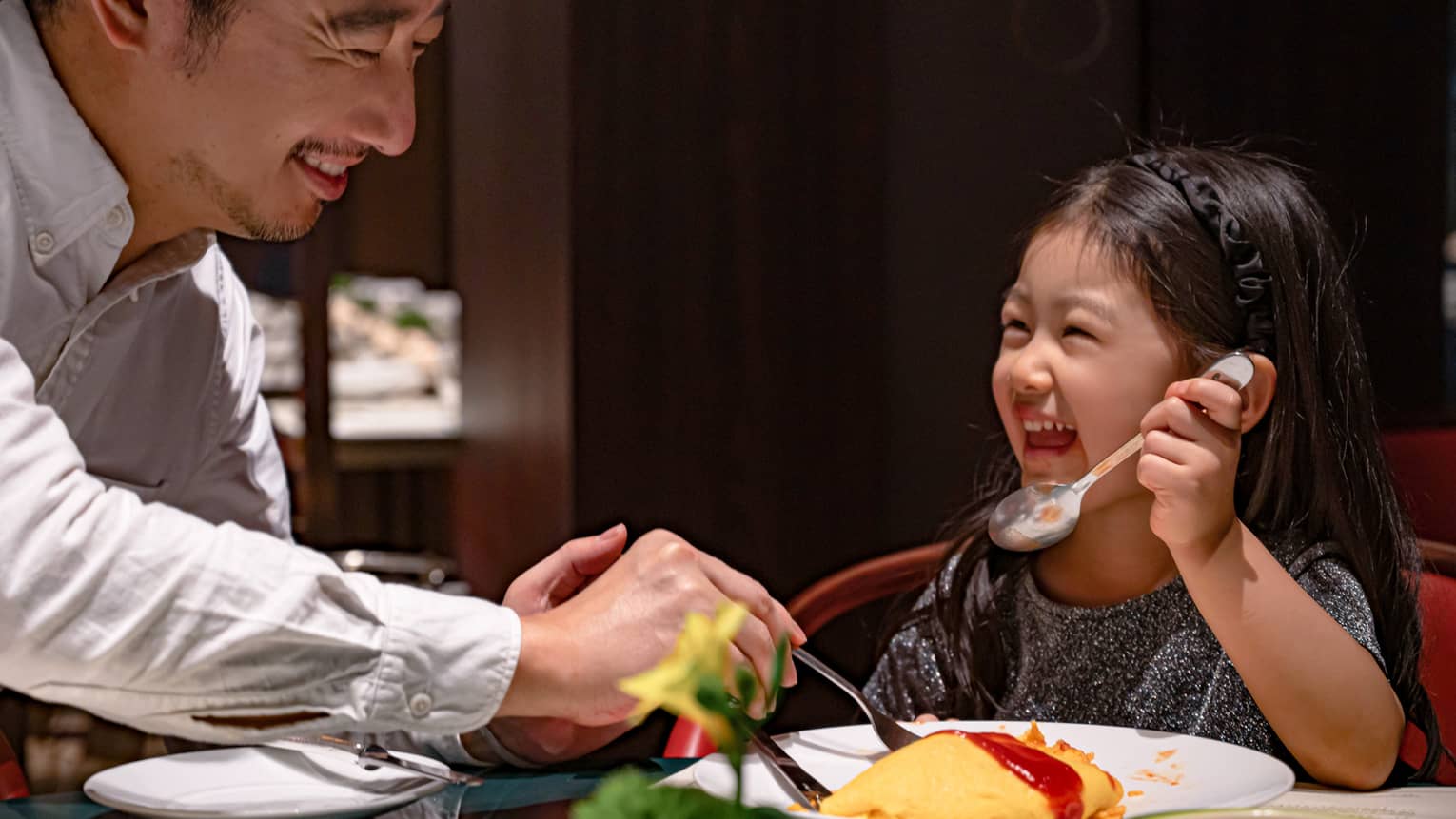 Smiling young girl and her dad dig into omurice topped with ketchup