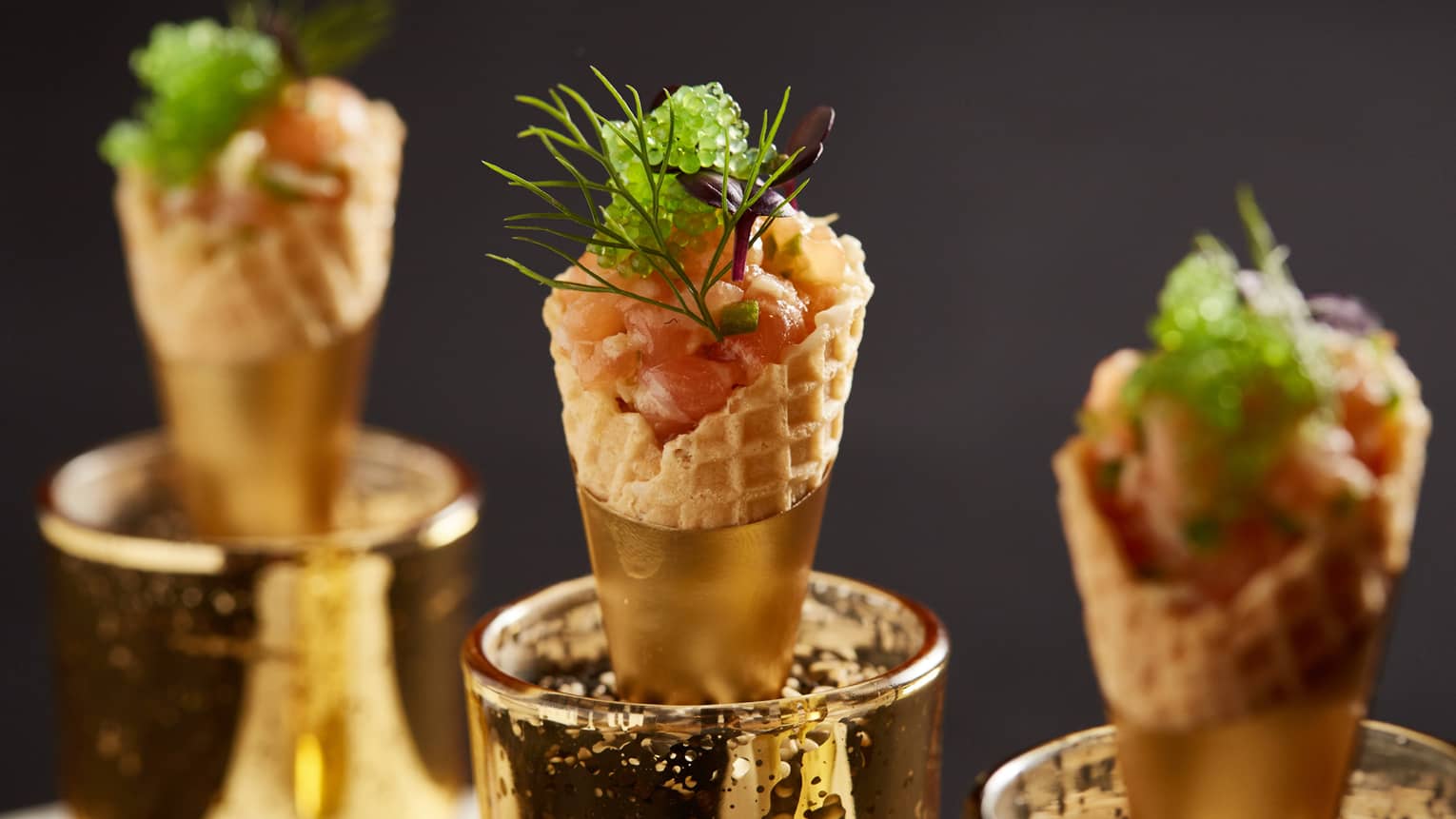 Three gold-rimmed cones filled with chopped fish and topped with caviar, herbs