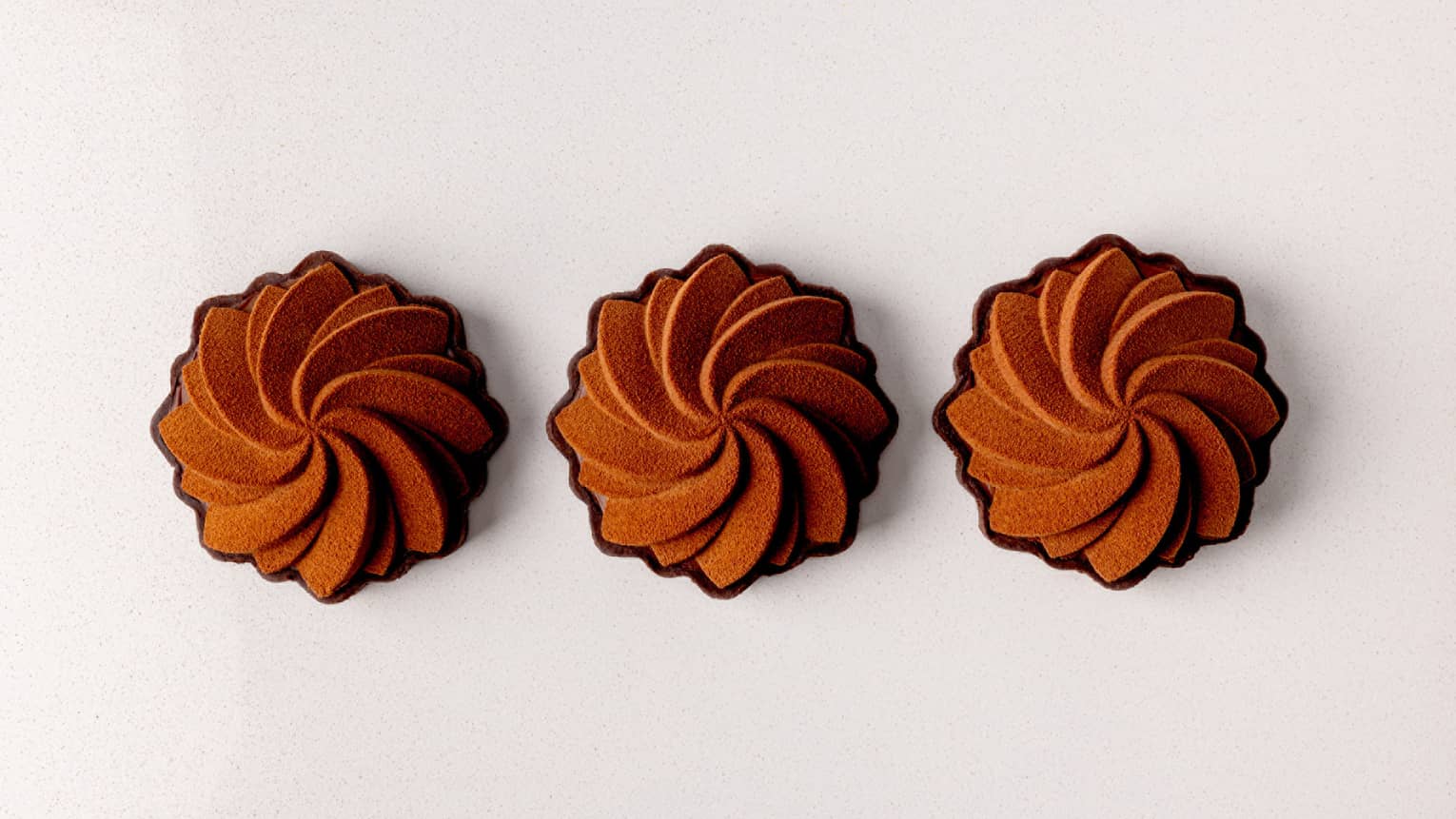 Three chocolate pastries lined up in a row on a white background