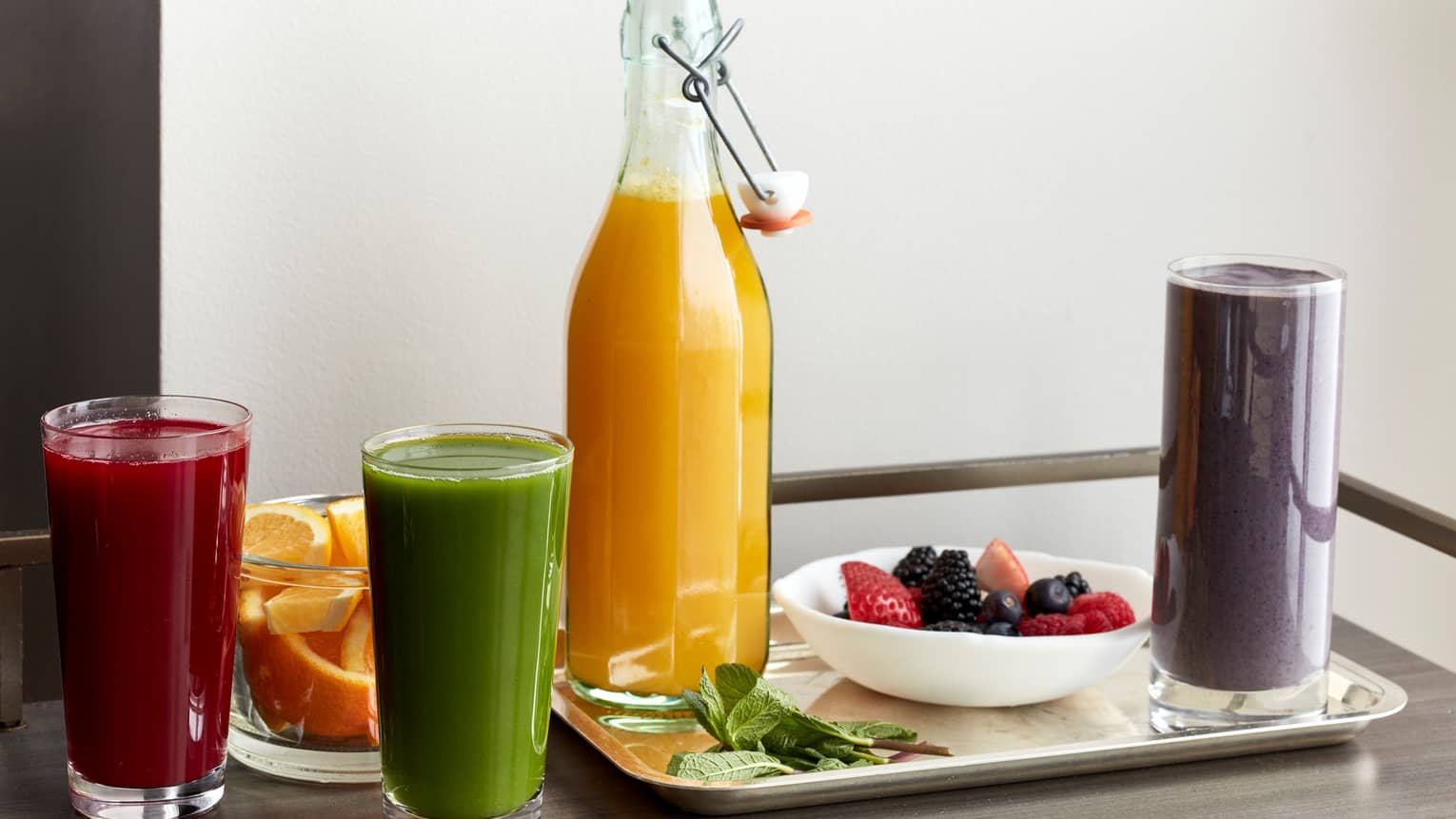 A table filled with various smoothies, a fruit bowl, and a bottle of orange juice