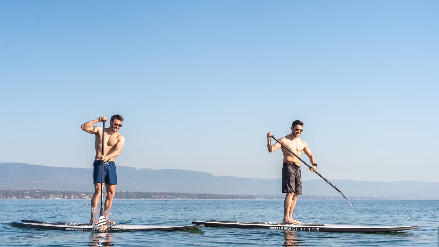 Two men stand-up paddleboarding on Lake Geneva