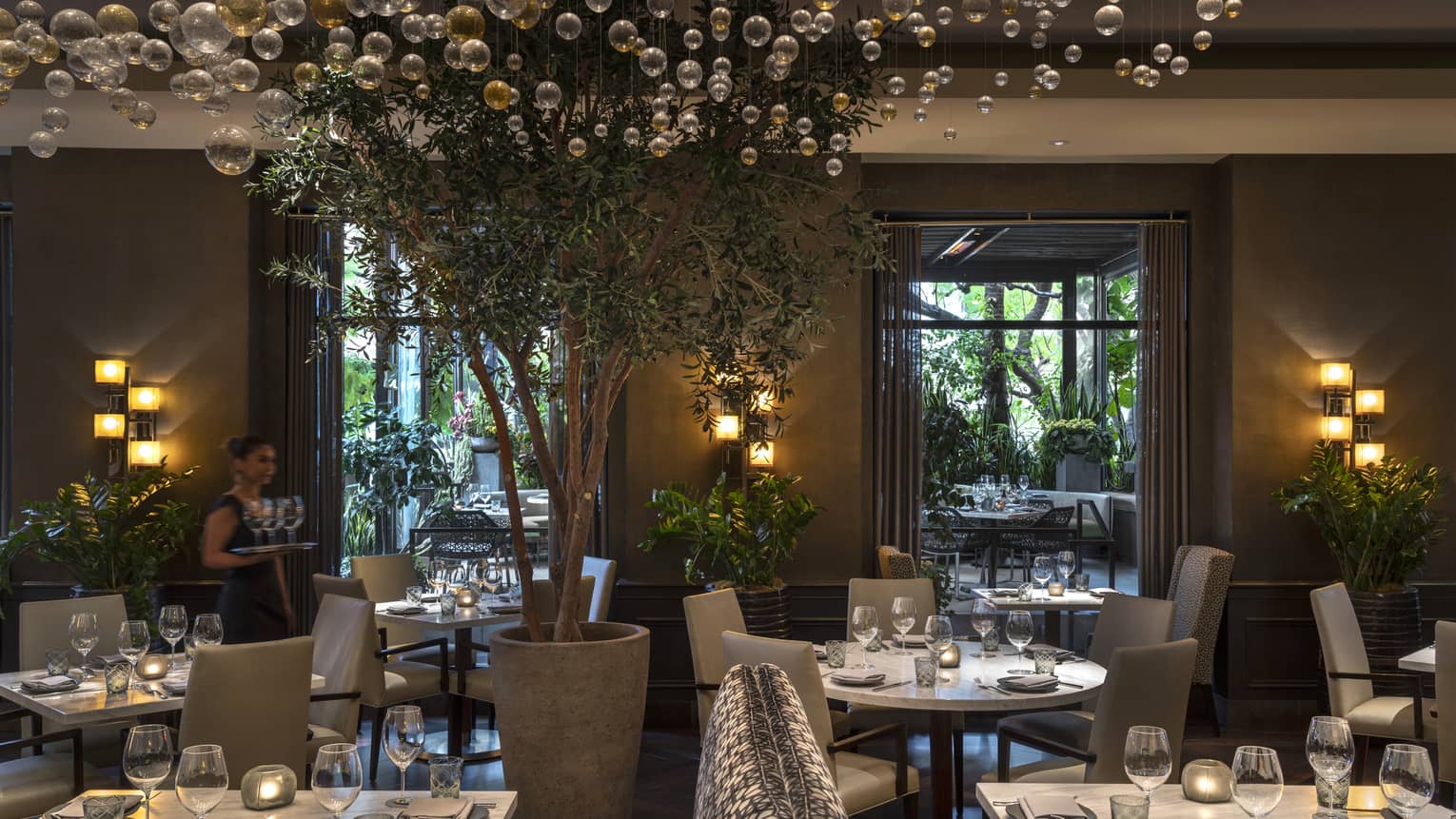 The interior of a dimly lit restaurant with white tables and grey chairs and bubble glass hanging like a chandelier.