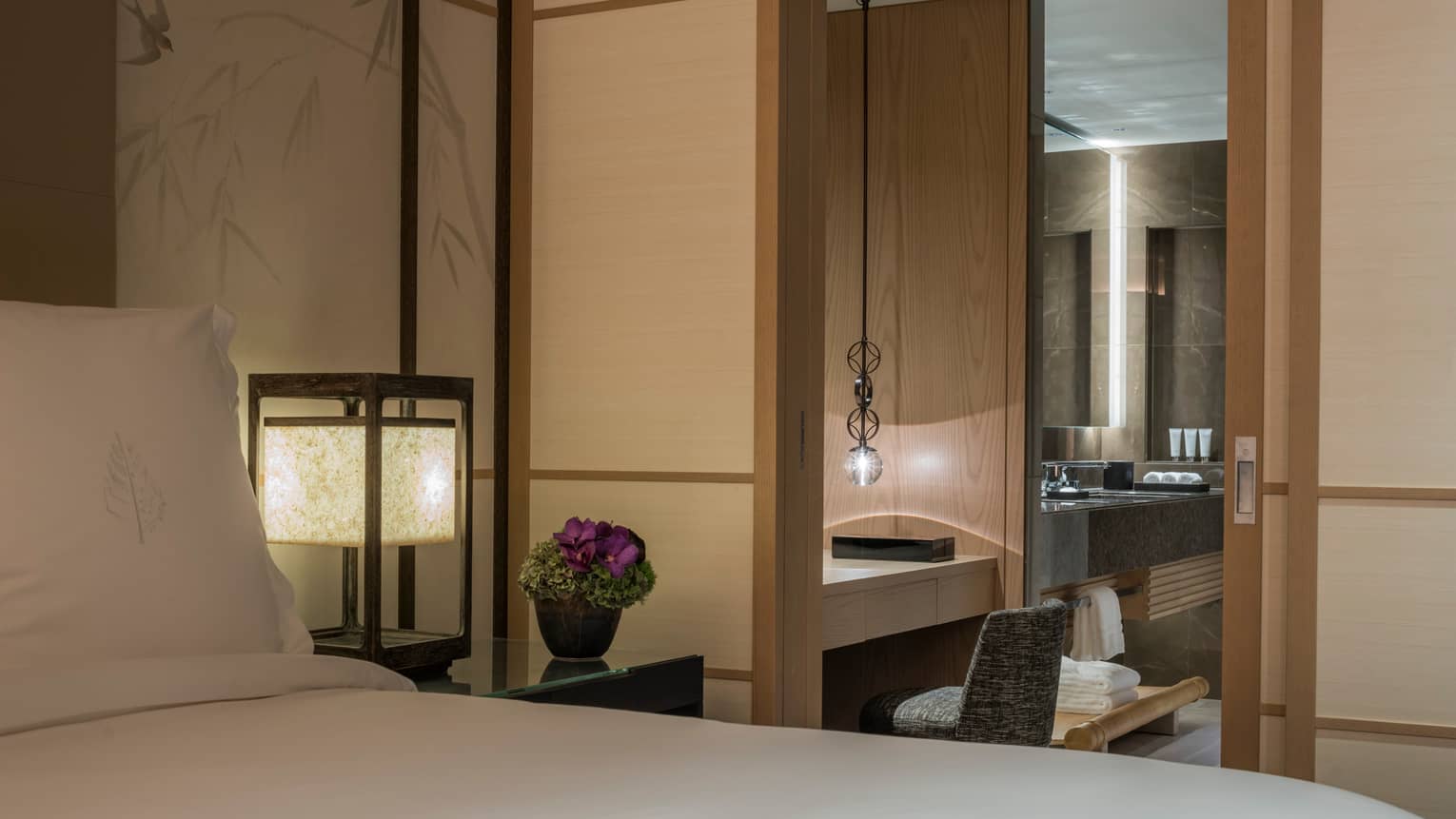 Bedroom view with sliding doors opening into a modern bathroom, featuring soft lighting and elegant Four Seasons décor