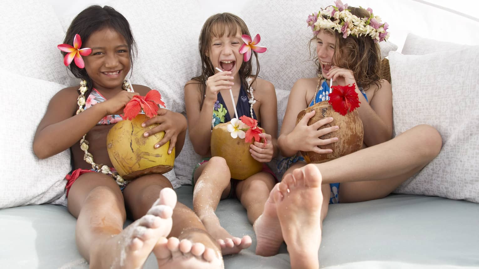 Three young girls laughing with tropical drinks, tropical flowers in their hair