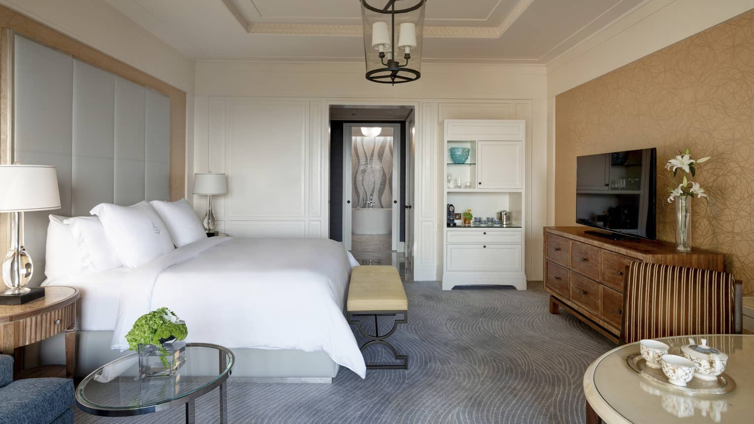 Bedroom with white-sheet bed, large grey headboard, wooden dresser