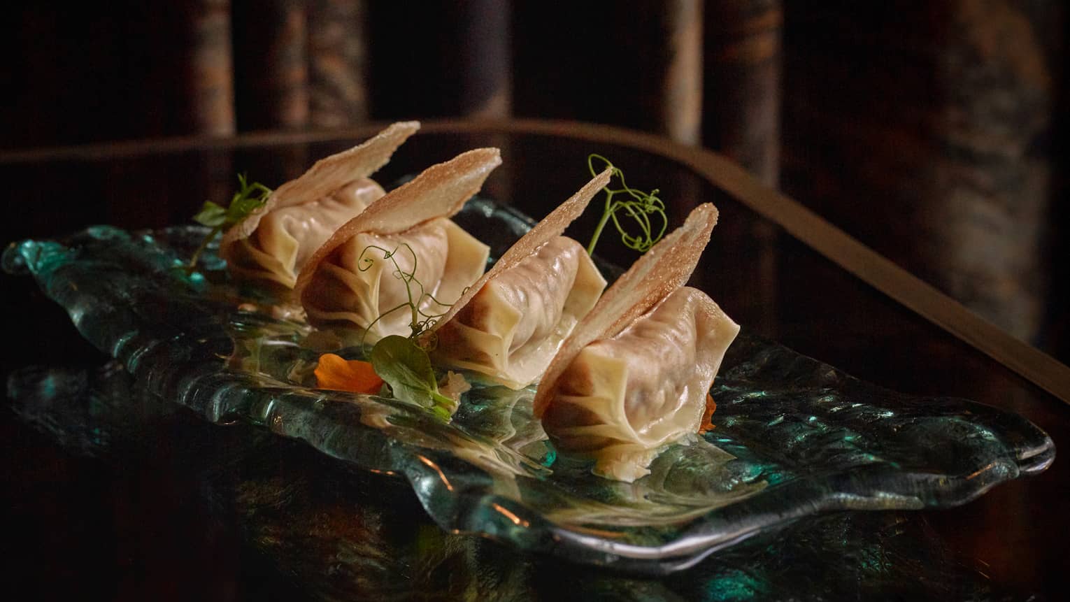 Four Gyoza in a row on green garnish on rectangular dish