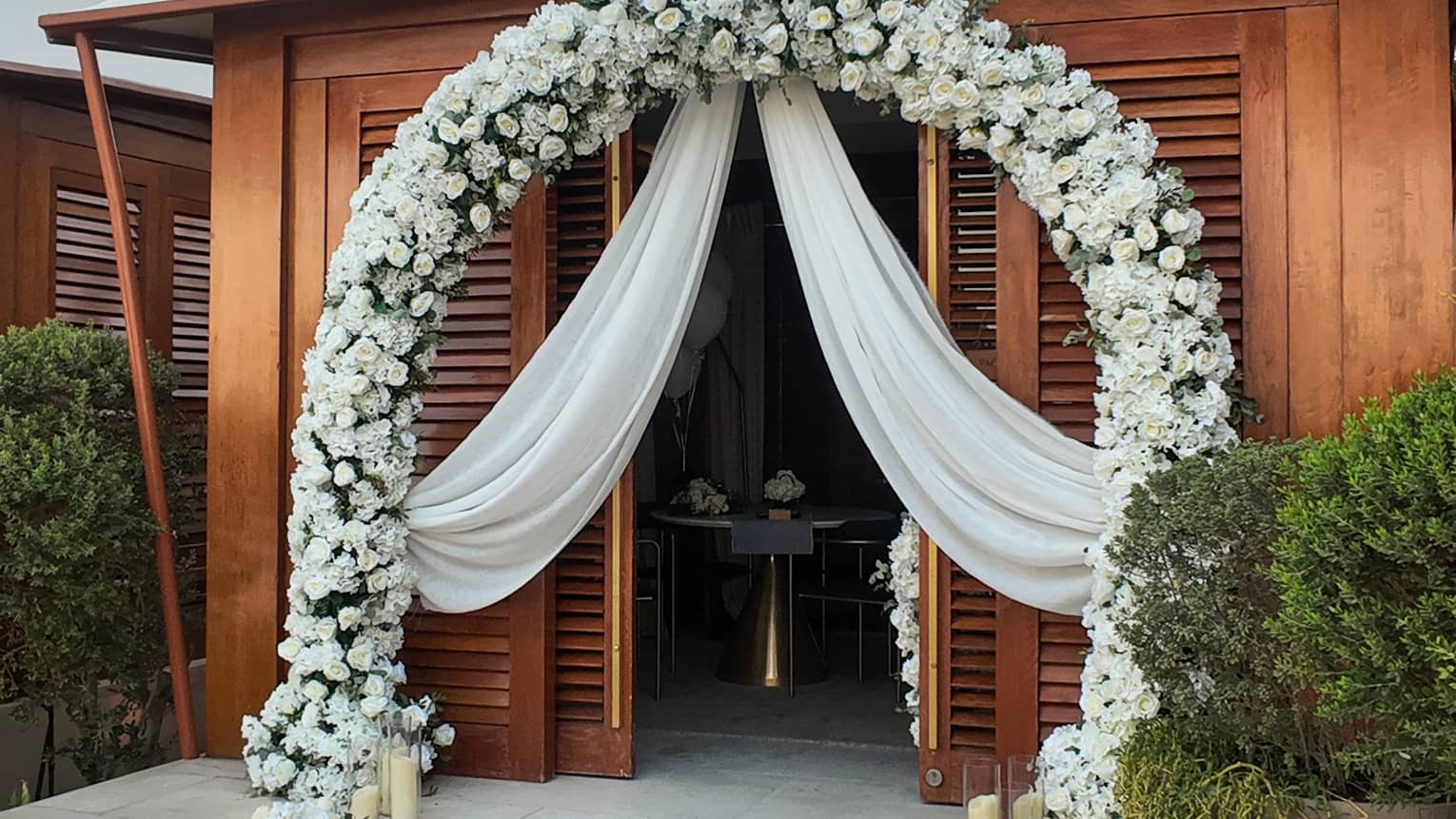 Poolside cabana decorated with a red carpet on the stairs and a large white floral arch way and curtains draping over the entrance