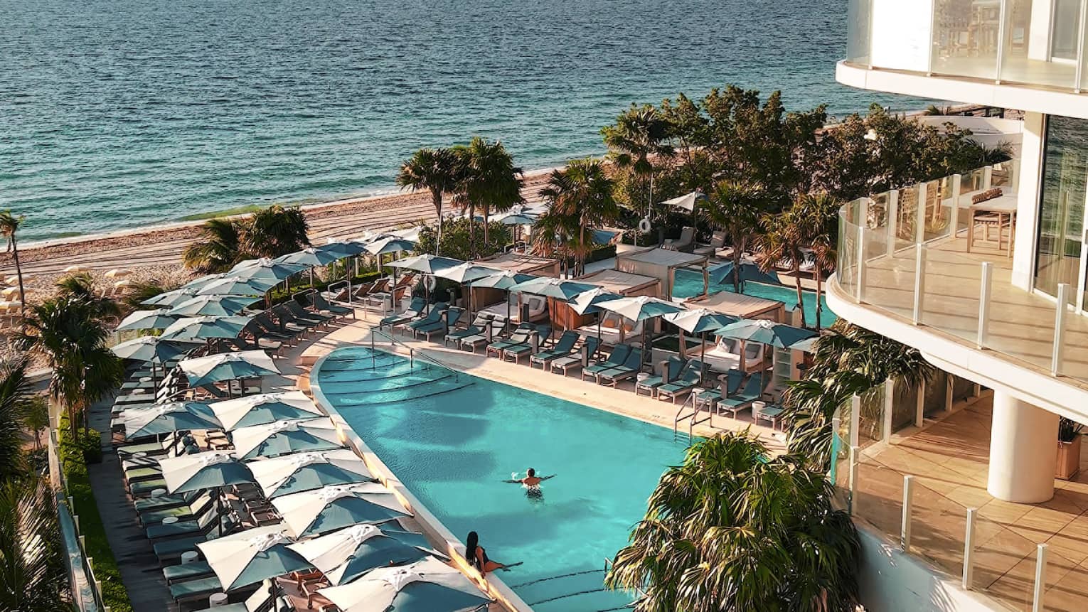 Two outdoor pools set between a hotel and the beach