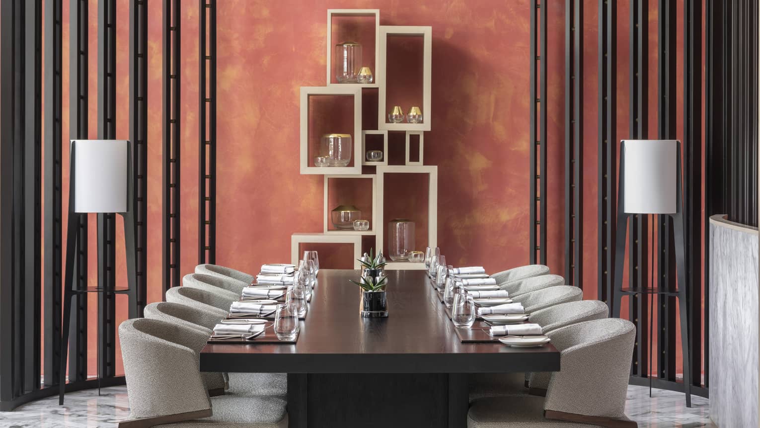 A sculptural lighting fixture hangs above a set table in a coral dining room