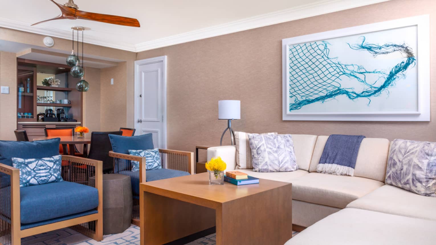 Oceanfront prime suite living area with cream-colored sofa, blue accent chairs, table, abstract wall art and dining area in the background