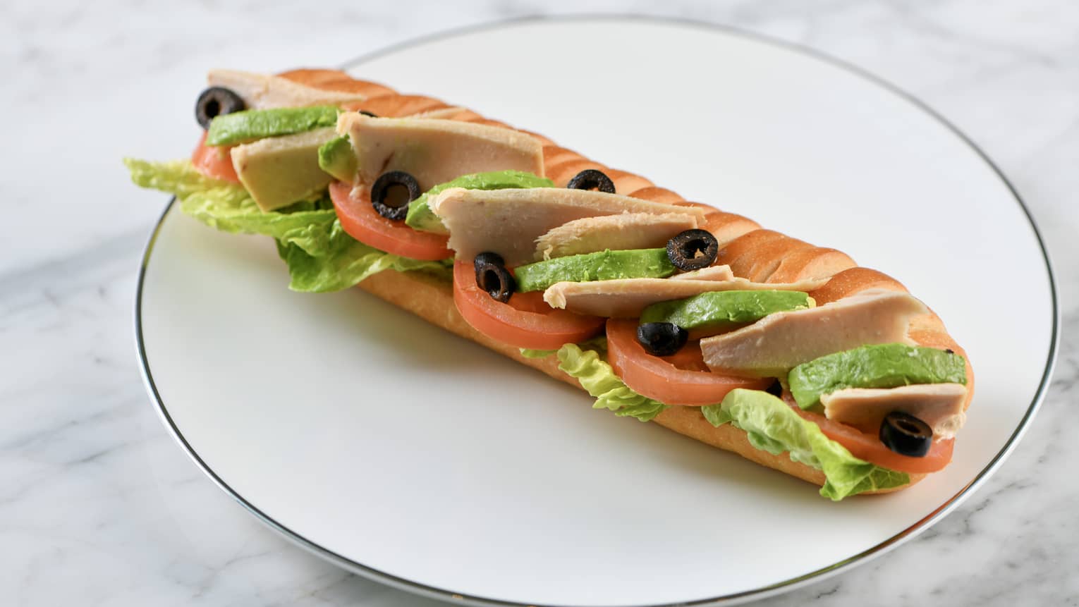 Sliced tuna, avocado, tomato, black olives and lettuce on a baguette