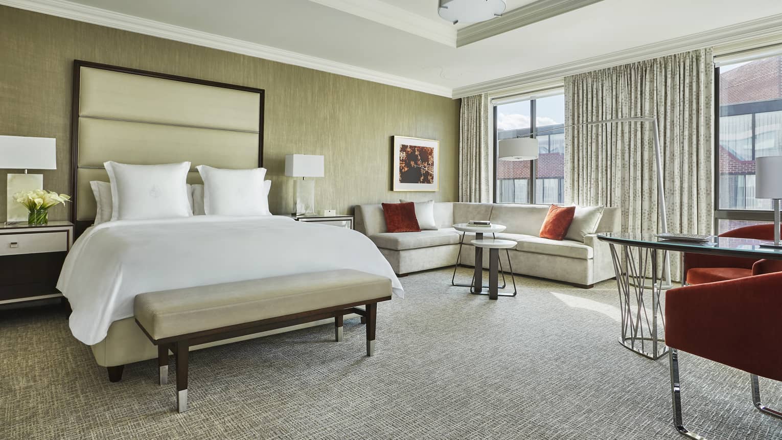 Grand Premier Room bed with white bench, tall padded headboard, L-shaped sofa near sunny picture window