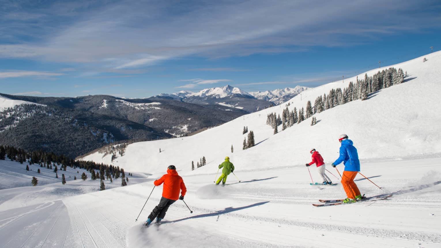 Four skiers in brightly coloured coats ski down mountain covered in snow