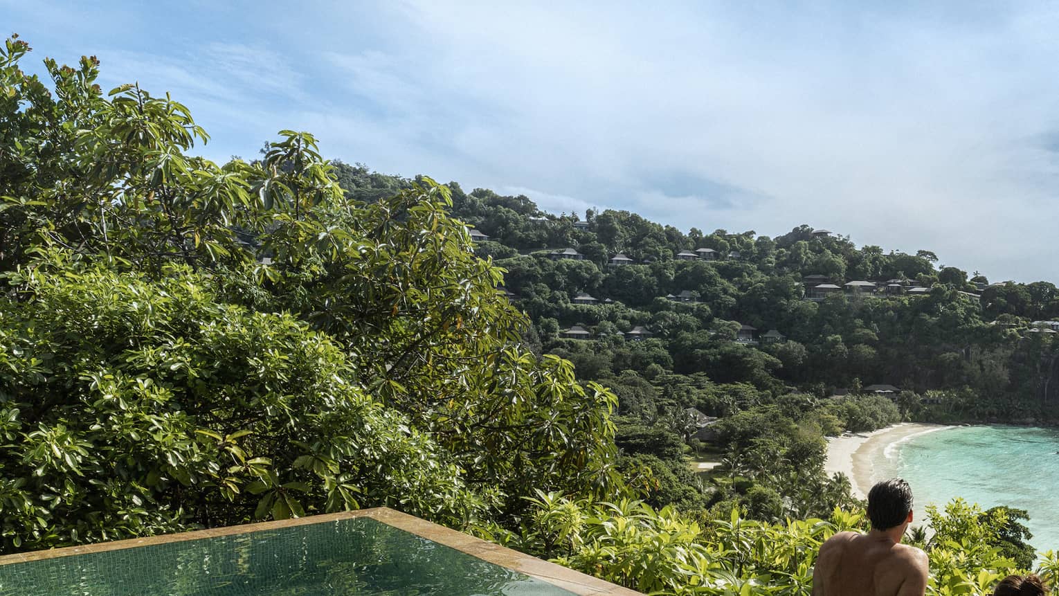 A couple looks out at a view of crystal blue waters and cliffs from an infinity pool