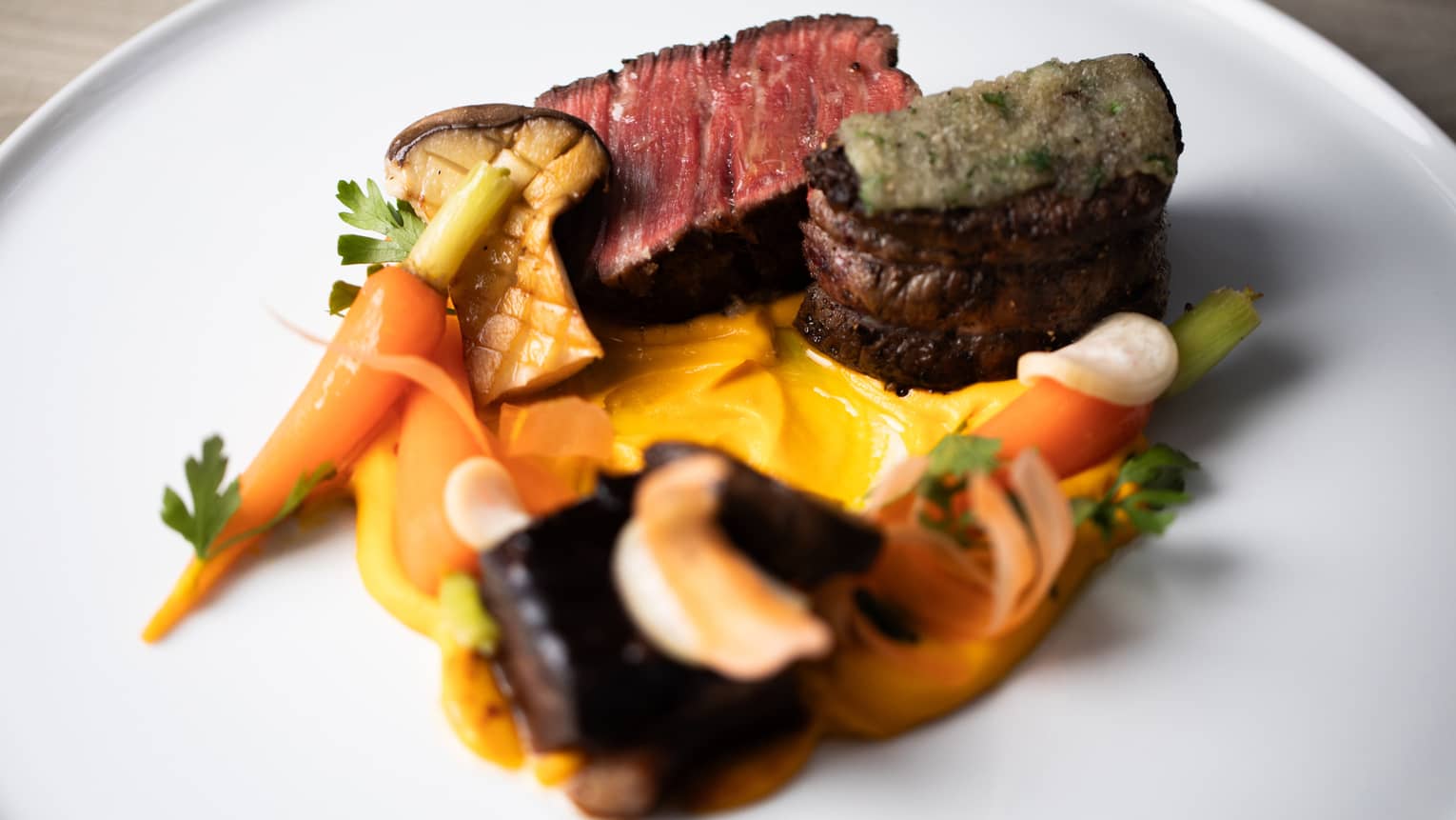 Slices of steak plated with grilled carrots, mushrooms and assorted vegetables